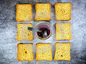 Flat lay of teaspoon dipped in a jar of grape jelly with rusks around