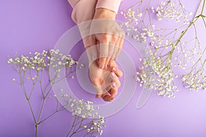 Flat lay. Tender female hands with white delicate flowers. On a purple background. Art photo, top view, horizontal photo