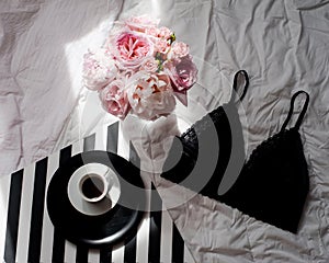 Flat lay. Top view black lace lingerie. Beauty blog concept. Bouquet of roses and pions, coffee on white bed background