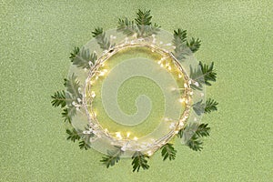 Flat lay top view, Christmas background circle shape border frame, light garland and fir twigs green glitter background