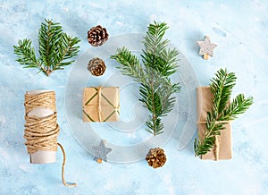 Flat lay top view christmas tree branches with toys, fir-cones and gifts in craft paper on blue background. New year holiday