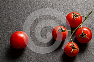 Flat lay, top view. Close up, macro. A sprig of juicy cherry tomatoes. Nearby is one red tomato. Black background. Copy space