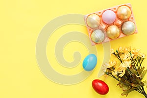 Flat lay top view colorful easter egg painted in pastel colors composition and spring flowers on yellow pastel color background.