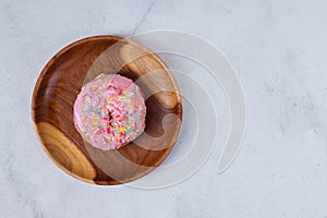 Flat lay top view of delicious sweet strawberry pink donut with sprinkles served on wooden plate. Isolated image on white