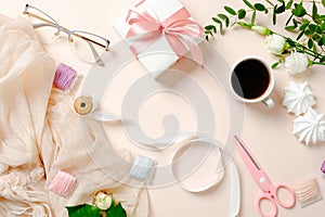 Flat lay, top view feminine desk with coffee cup, flowers, marshmallows, gift box and spools with ribbon on pink background.