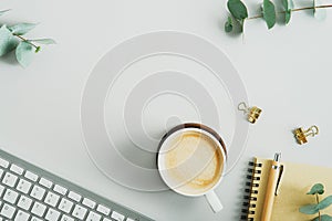 Flat lay top view feminine workspace with coffee cup, keyboard, office supplies, eucalyptus branches on green background. Home