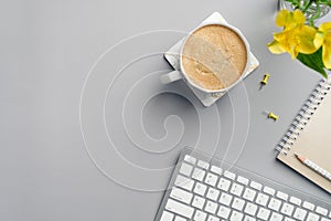 Flat lay top view home office desk. Modern workspace with cup of coffee, yellow office supplies, flower, keyboard on grey