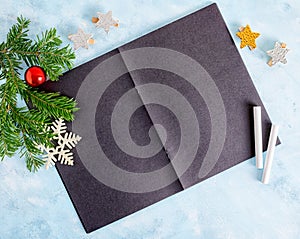 Flat lay top view mock up: christmas tree branches with toys, open black notebook and chalk