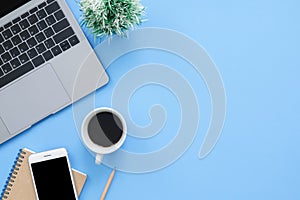 Flat lay top view mockup photo of working space with laptop, smartphone, coffee up and notebook on blue pastel background.