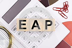 Flat lay, top view of office desk. Workspace with white calculator, magnifying glass, red paper clips and wooden cubes with EAP