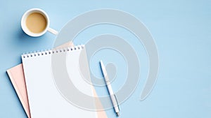 Flat lay, top view office table desk. Workspace with blank paper notepad, cup of coffee and pen on blue background. Feminine