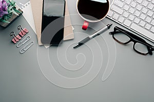 Flat lay, top view office table desk. Workspace with keyboard, office supplies, pencil, green leaf, and coffee cup on gray