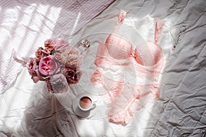 Flat lay. Top view pink lace lingerie. Beauty blog. Bouquet of roses and pions, parfume, jewelry, coffee on white bed background