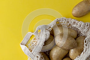 Flat lay top view raw organic potatoes in string bag on yellow background