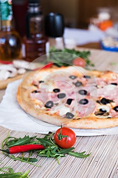 Flat lay with traditional Italian pizza with ham and olives on black stone table and various ingredients