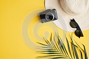 Flat lay traveler accessories on yellow background. Top view female beach hat, vintage camera, sunglasses, palm leaf. Travel or