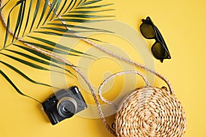 Flat lay traveler accessories on yellow background. Top view palm leaf, rattan straw bag, photo camera, sunglasses. Travel or