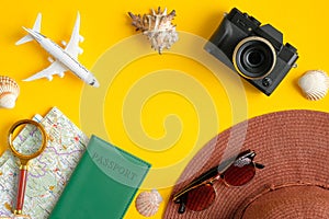Flat lay traveler accessories on yellow background with vintage camera, airplane model, beach hat, passport, map, magnifying glass