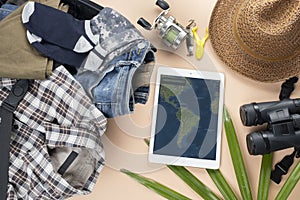 Flat lay travelling set with spinning of fishing tools, binoculars, hat, man cloths and gadget with map on pastel background.