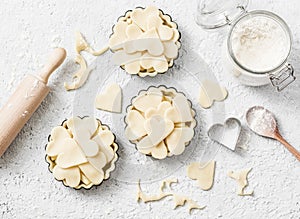 Flat lay Valentine`s day baking background. Raw apple tartlets in the baking dish and baking ingredients on light background