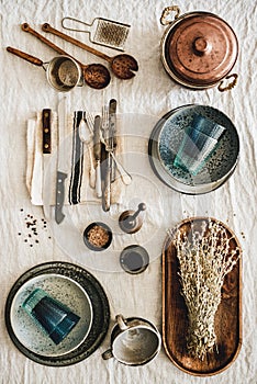 Various kitchen utensils and tablewear over linen tablecloth, vertical composition photo