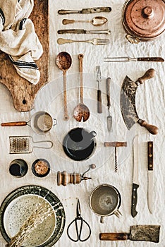 Various kitchen utensils and tablewear over linen tablecloth, vertical composition