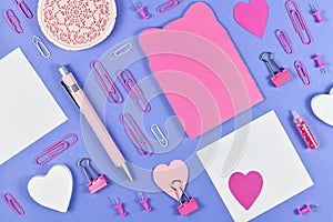 Flat lay with various pink arranged office supplies like pen, note book, blank note paper, pins or retaining clip on  purple backg