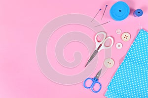 Flat lay with various sewing tools like fabric, scissors, buttons or pins on pink background with blank copy space