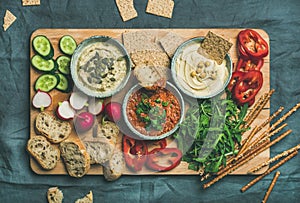 Flat-lay of Vegetarian dips hummus, babaganush, muhammara on wooden board