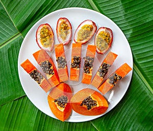 Flat lay. Vegetarian nutrition. papaya pieces and passion fruit on white plate with green banana leaves background, top view