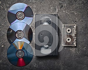 Flat lay video cassettes, CD's, audio cassette on a black concrete surface. Retro media technology of the past.