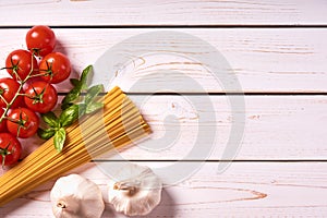 Flat lay view of pasta or spaghetti with bunch of tomatoes, garlic and basil leaves. Old white wooden background or table top