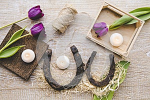 Flat lay view of two rusty small and big horseshoes on light wooden board background, decorated with white small candles.