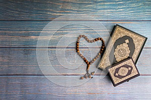 Flat lay view of vase, tasbih or rosary beads and Holy book of Quran with arabic calligraphy meaning of Al Quran over wooden backg