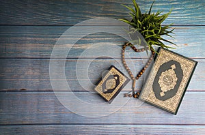 Flat lay view of vase, tasbih or rosary beads and Holy book of Quran with arabic calligraphy meaning of Al Quran over wooden backg