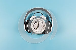 Flat lay of vintage alarm clock show 7 o`clock cover with headphones on blue  background ,time to listen to music concept or