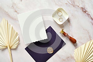 Flat lay wedding stationery on marble table. Blank wedding invitation card mockup, dried flowers, rings, purple envelope, wax seal