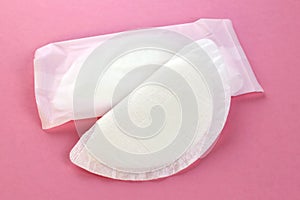 A flat lay of white absorbent nursing pads on an pink background