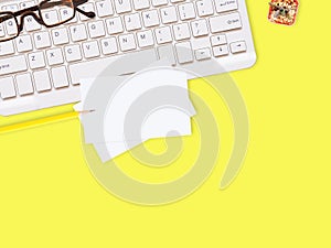 Flat lay white business card over keyboard with glasses, pencil, and cactus on yellow office desktop with copy space for text.