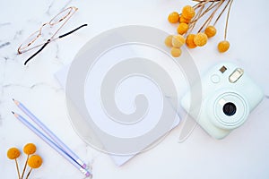 Flat lay of white marble table with stationery, glasses, yellow flowers and photo camera