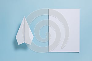 Flat lay of white paper plane and blank paper on pastel blue col