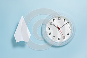 Flat lay of white paper plane and wall clock on pastel blue color background