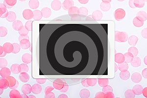 Flat lay of white touchpad with blank screen on pink confetti background