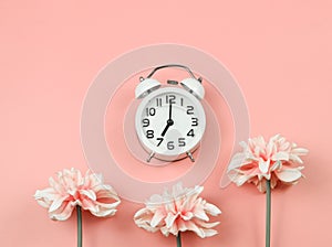 Flat lay of white vintage alarm clock  with pink flowers decoration  on pink background