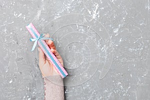 Flat lay of woman hands holding gift wrapped and decorated with bow on gray cement wooden background with copy space. Christmas