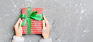 Flat lay of woman hands holding gift wrapped and decorated with bow on gray cement wooden background with copy space. Christmas