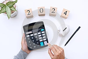 Flat lay woman hands using calculator with number 2024 on white desk. New year goals, Business and finance planing concept. Copy