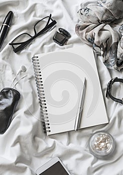 Flat lay women accessories background. Blank notepad, pen, glasses, watch, mascara, phone, headphones, perfume on a light backgrou