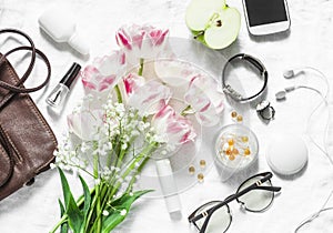 Flat lay women`s accessories set-leather bag, tulips bouquet, cosmetics, glasses, phone, apple, headphones on light background