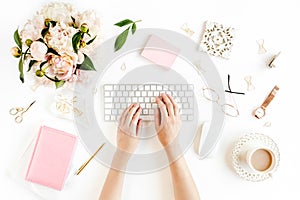 Flat lay women`s office desk. Female workspace with female hands, computer, pink peonies bouquet, accessories on white